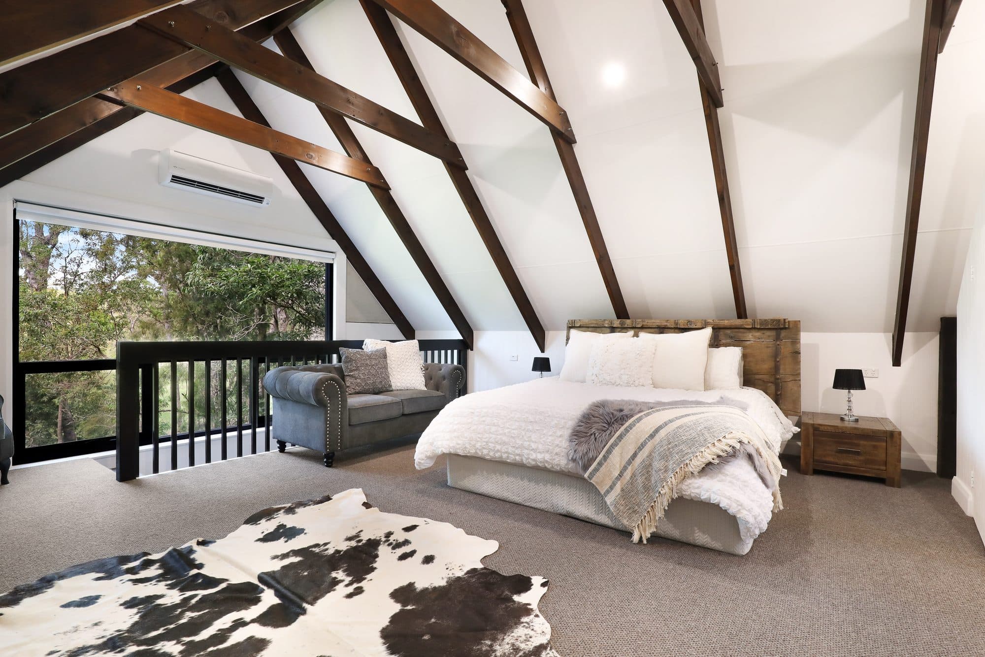 Bedroom at Levante, Serenity 222 — dark timber beams and a cowhide rug among the gum trees